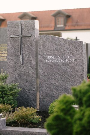 Zweiteiliger Grabstein aus dunkelgrauem Granit mit geschroteter Oberfläche und modernem Metallkreuz