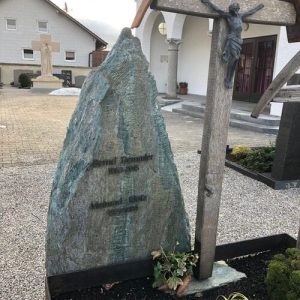 Natürlicher Felsblock als Grabmal mit Holzkreuz und Jesus-Figur auf Dorffriedhof