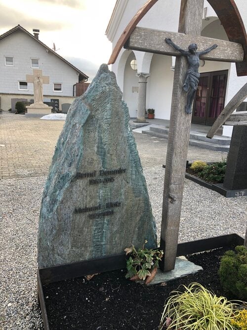 Natürlicher Felsblock als Grabmal mit Holzkreuz und Jesus-Figur auf Dorffriedhof
