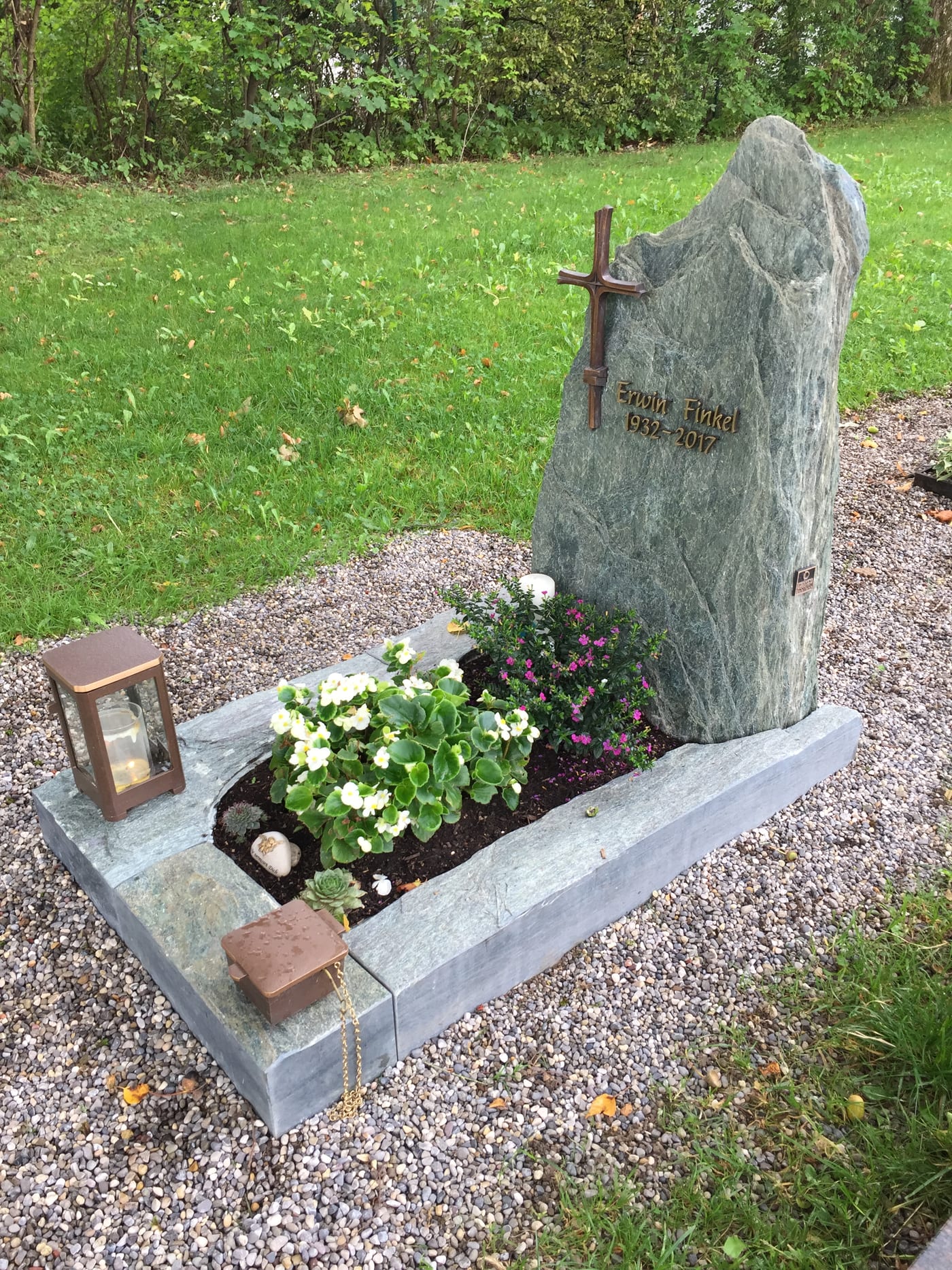 Grüner Serpentinit-Felsgrabstein in massiver organischer Form mit Metallkreuz und passender Grabanlage – Ansicht 2