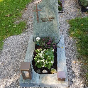 Grüner Serpentinit-Felsgrabstein in massiver organischer Form mit Metallkreuz und passender Grabanlage