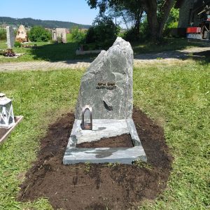Dunkelgrüner Naturstein-Felsgrabstein in kompakter organischer Form mit natürlicher Spaltbruchoberfläche und Schriftgravur