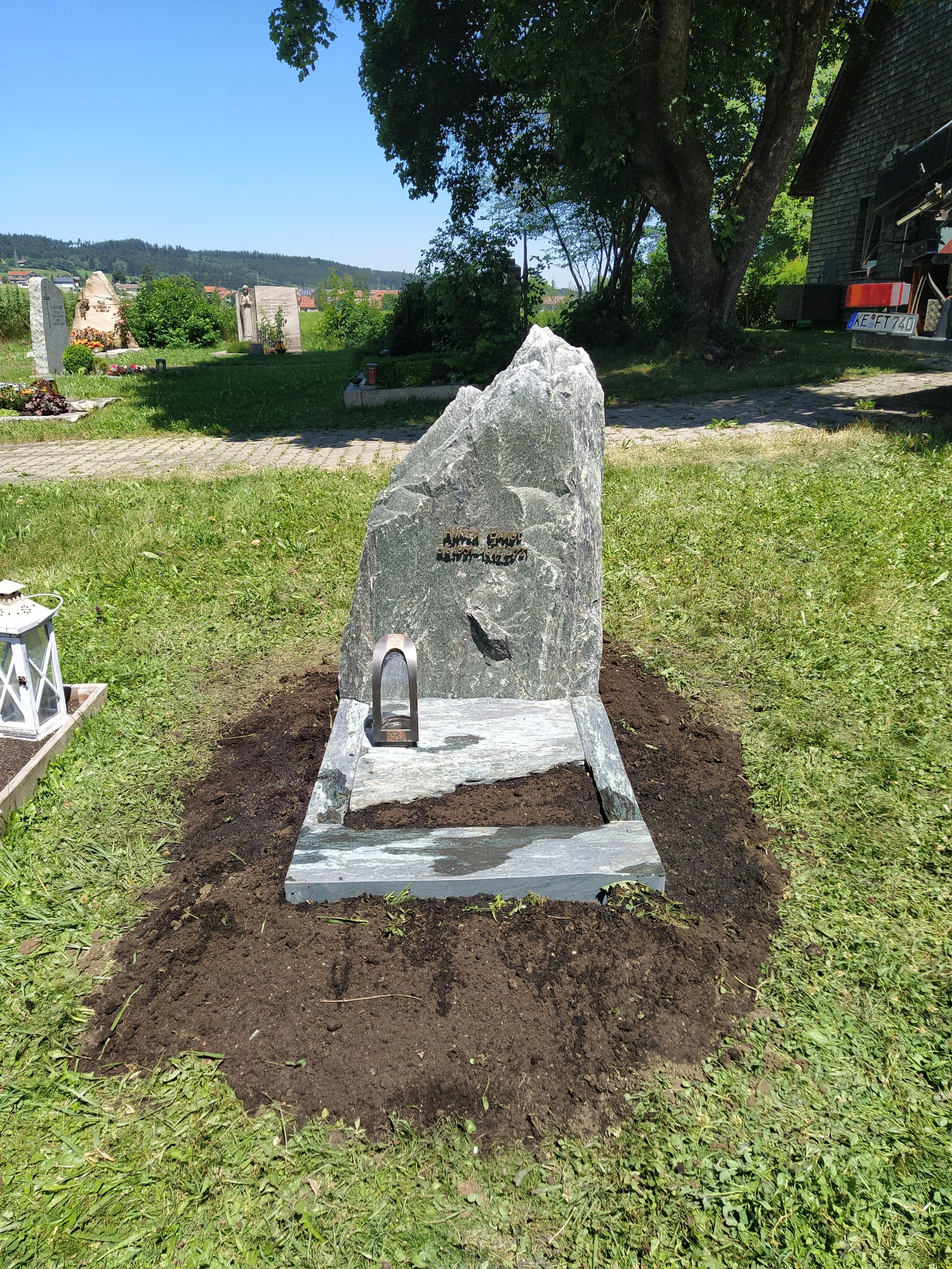 DunkelgrÃ¼ner Naturstein-Felsgrabstein in kompakter organischer Form mit natÃ¼rlicher SpaltbruchoberflÃ¤che und Schriftgravur