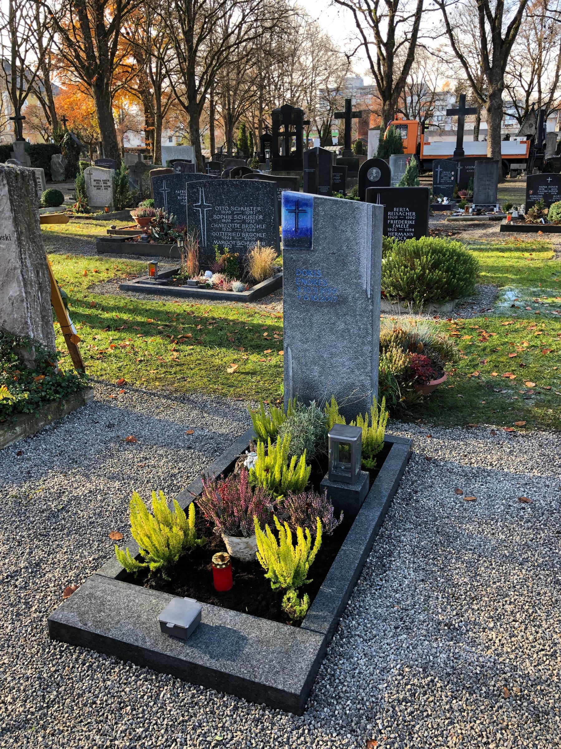 Grabstein aus grauem Granit mit rechteckiger blauer Glaseinlage und Kreuzornament in herbstlichem Friedhofsambiente