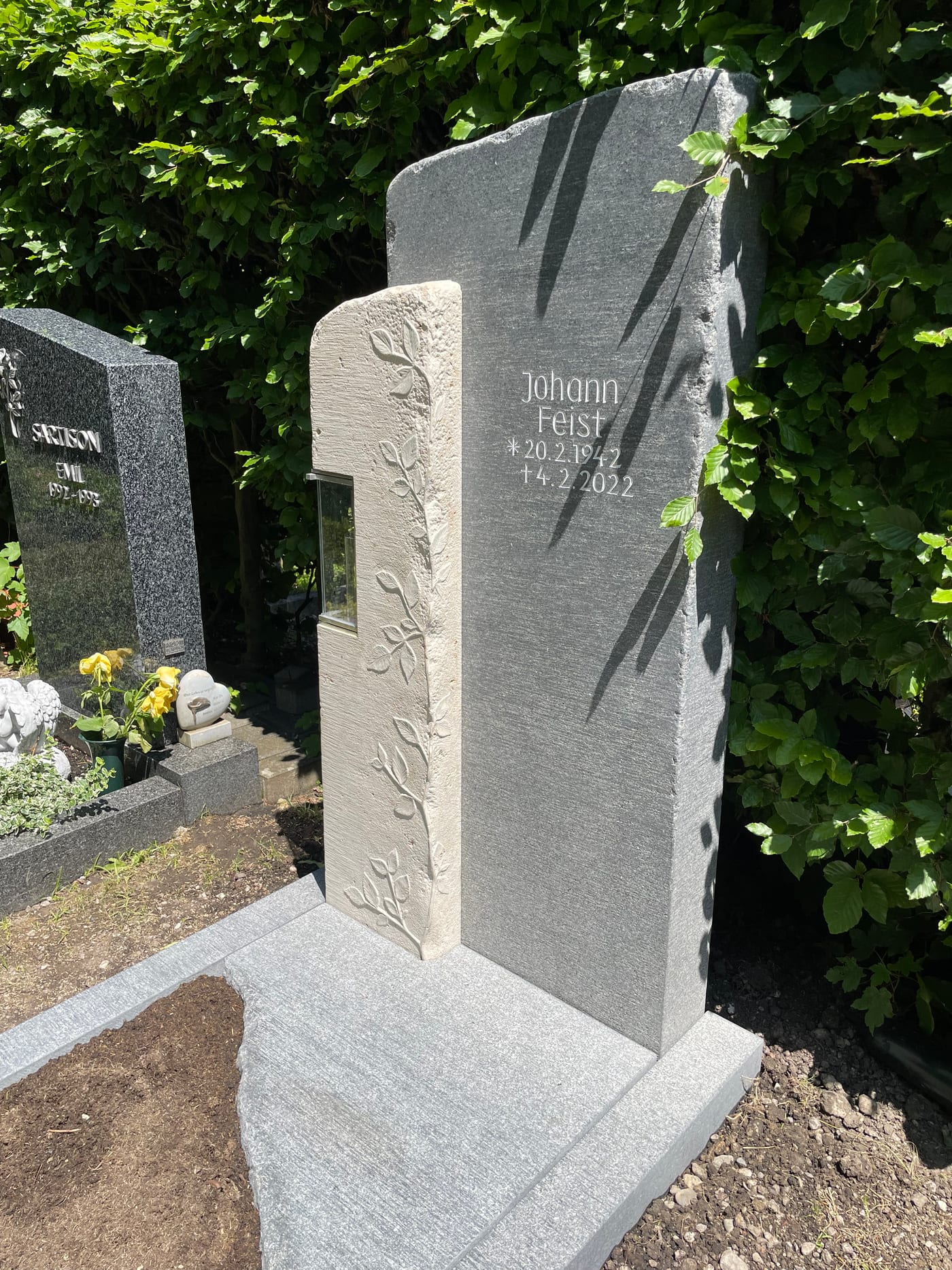 Zweiteiliger dunkelgrauer Granit-Grabstein mit filigranem Ranken-Relief und integrierter Kerze
