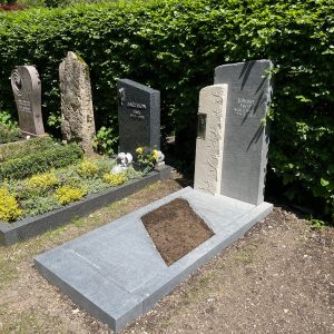 Zweiteiliger dunkelgrauer Granit-Grabstein mit filigranem Ranken-Relief und integrierter Kerze