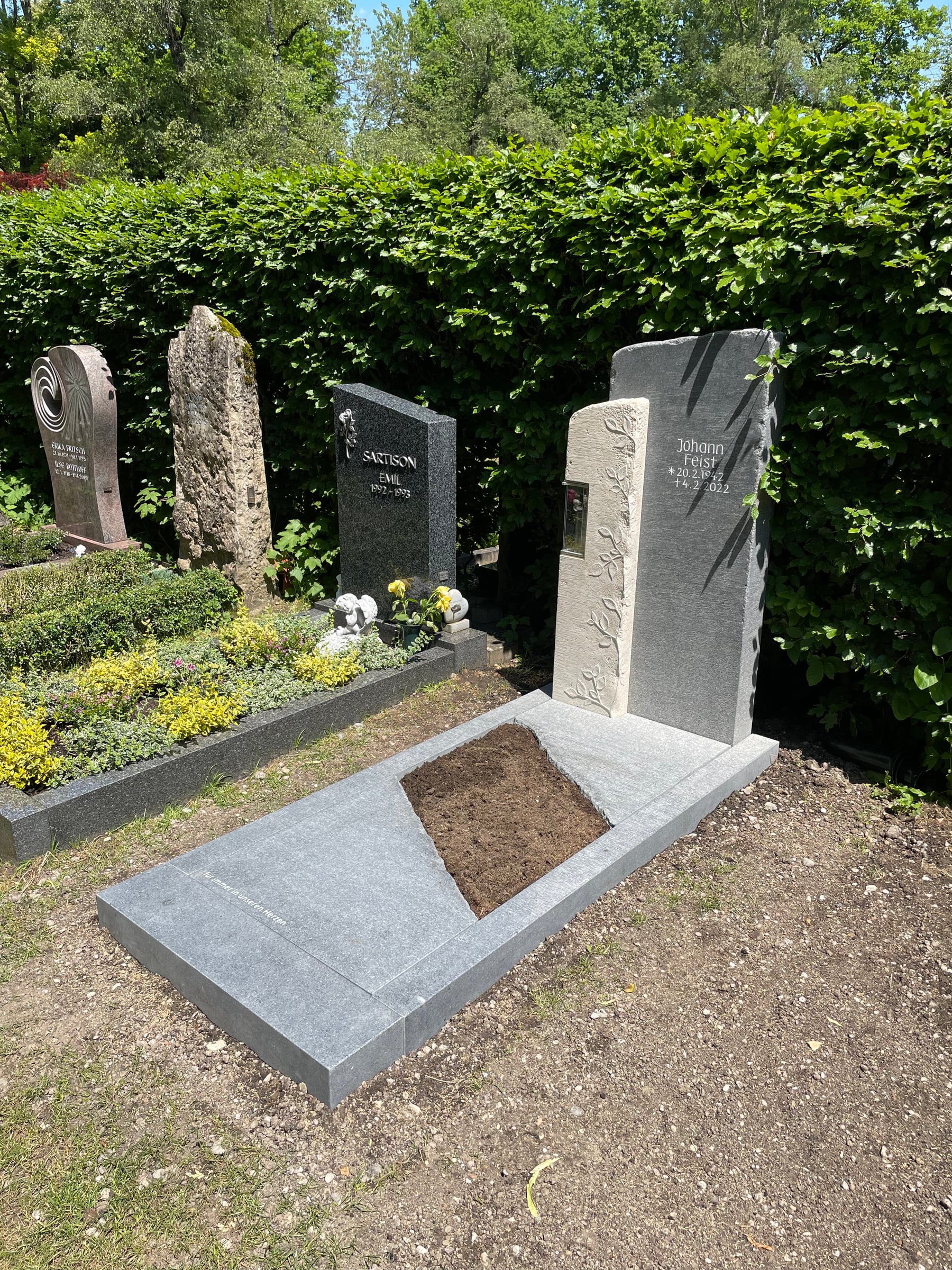 Zweiteiliger dunkelgrauer Granit-Grabstein mit filigranem Ranken-Relief und integrierter Kerze