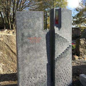 Mehrteiliger Grabstein aus dunklem Granit mit geometrischem Stufendesign und roter Glaseinlage