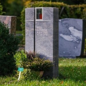 Grauer Granit-Grabstein mit vertikalem Kreuzschlitz und integrierter Glaskerze im oberen Bereich
