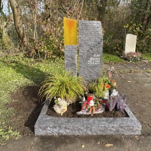 Moderner Grabstein aus dunklem Anthrazit-Granit mit leuchtend orangem Glas-Element und gestufter Oberkante