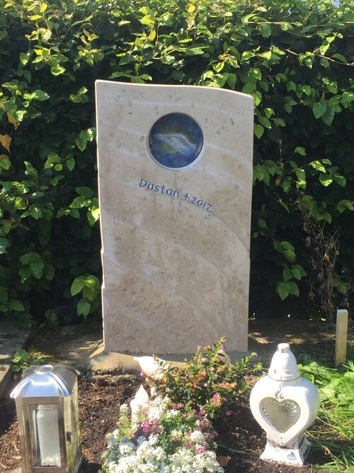 Kindergrabstein aus warmem Travertin mit runder Glaseinlage und blau-silbernem Engelsflügel-Motiv
