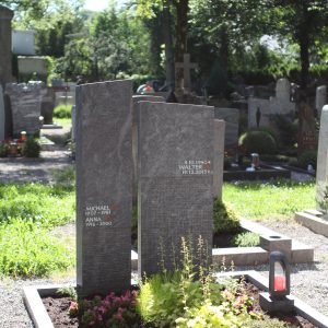 Zweiteiliges Doppelgrab-Grabmal aus dunklem Naturstein mit auffallender roter Schriftgravur