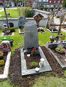 Naturbelassener dunkelgrüner Diabas-Felsstein mit Goldkreuz auf dem Friedhof – STOI Steinmetzwerkstatt