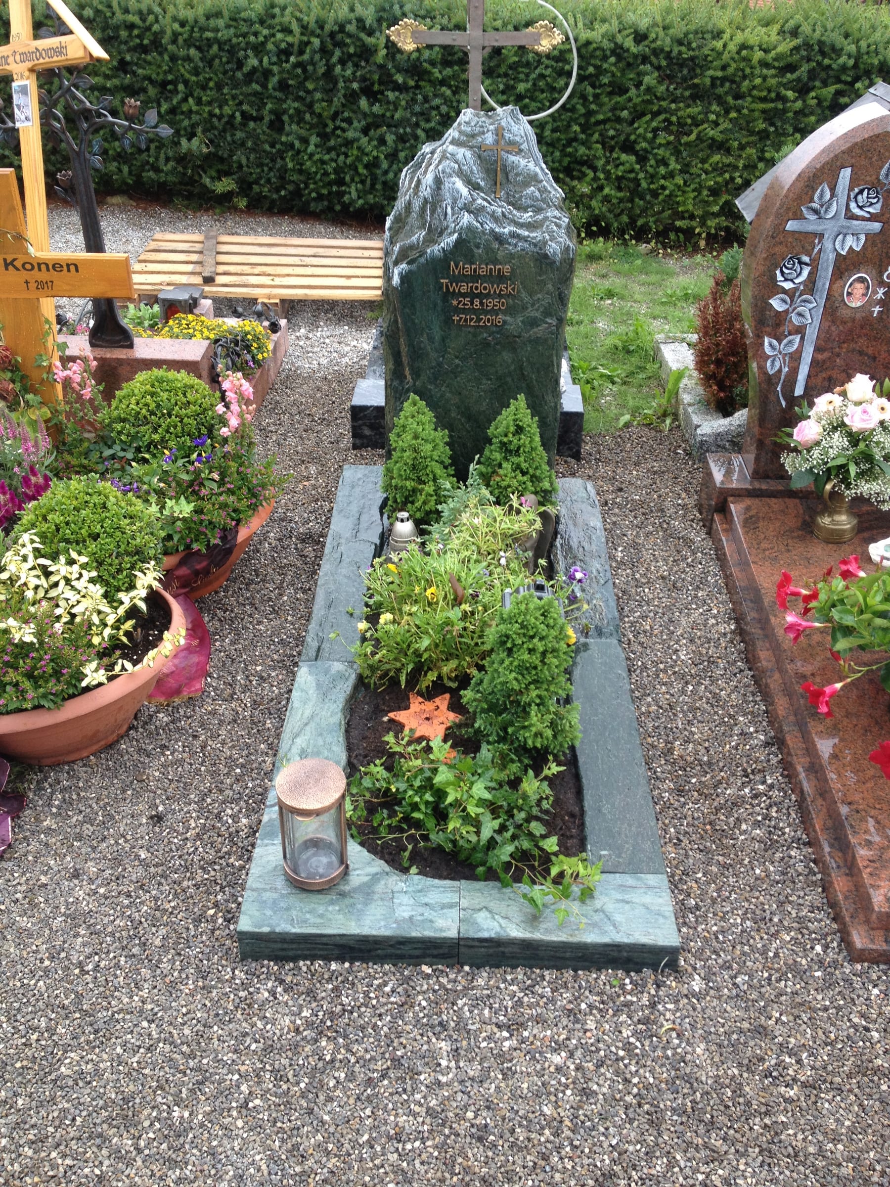 Felsengrabstein aus dunkelgrünem Naturstein in Bergform mit vergoldetem Kreuzornament an der Spitze