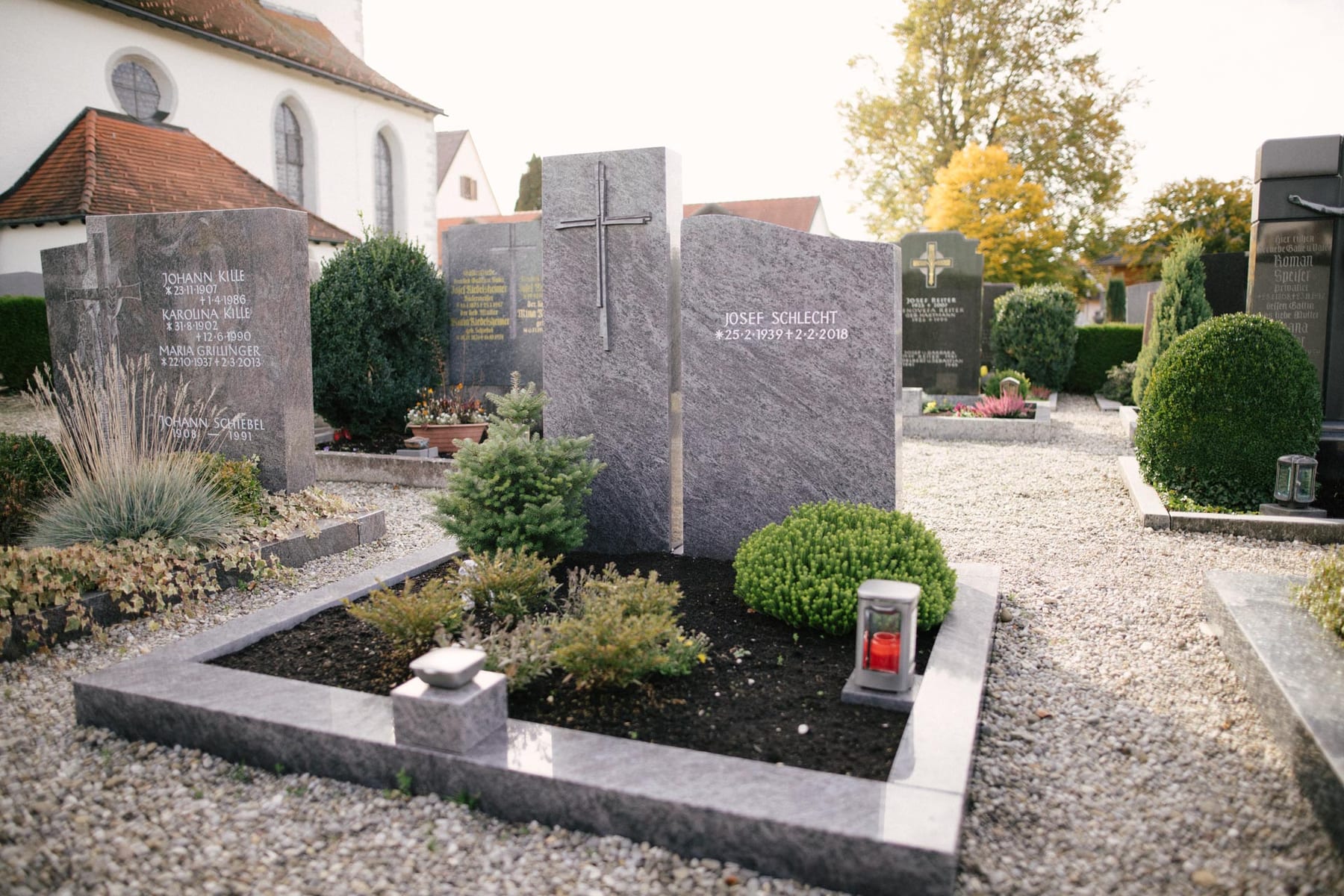 Zweiteiliger Grabstein aus dunkelgrauem Granit mit geschroteter Oberfläche und modernem Metallkreuz