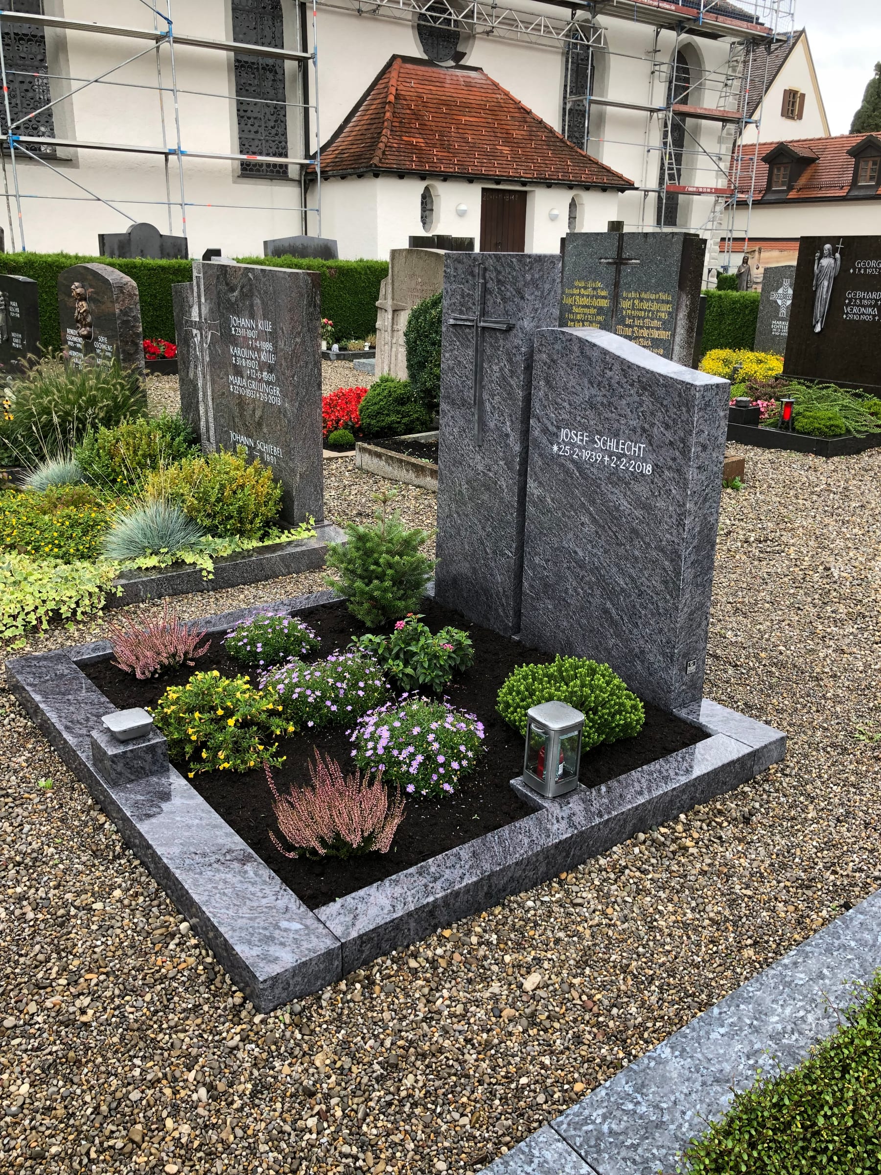 Zweiteiliger Grabstein aus dunkelgrauem Granit mit geschroteter Oberfläche und modernem Metallkreuz