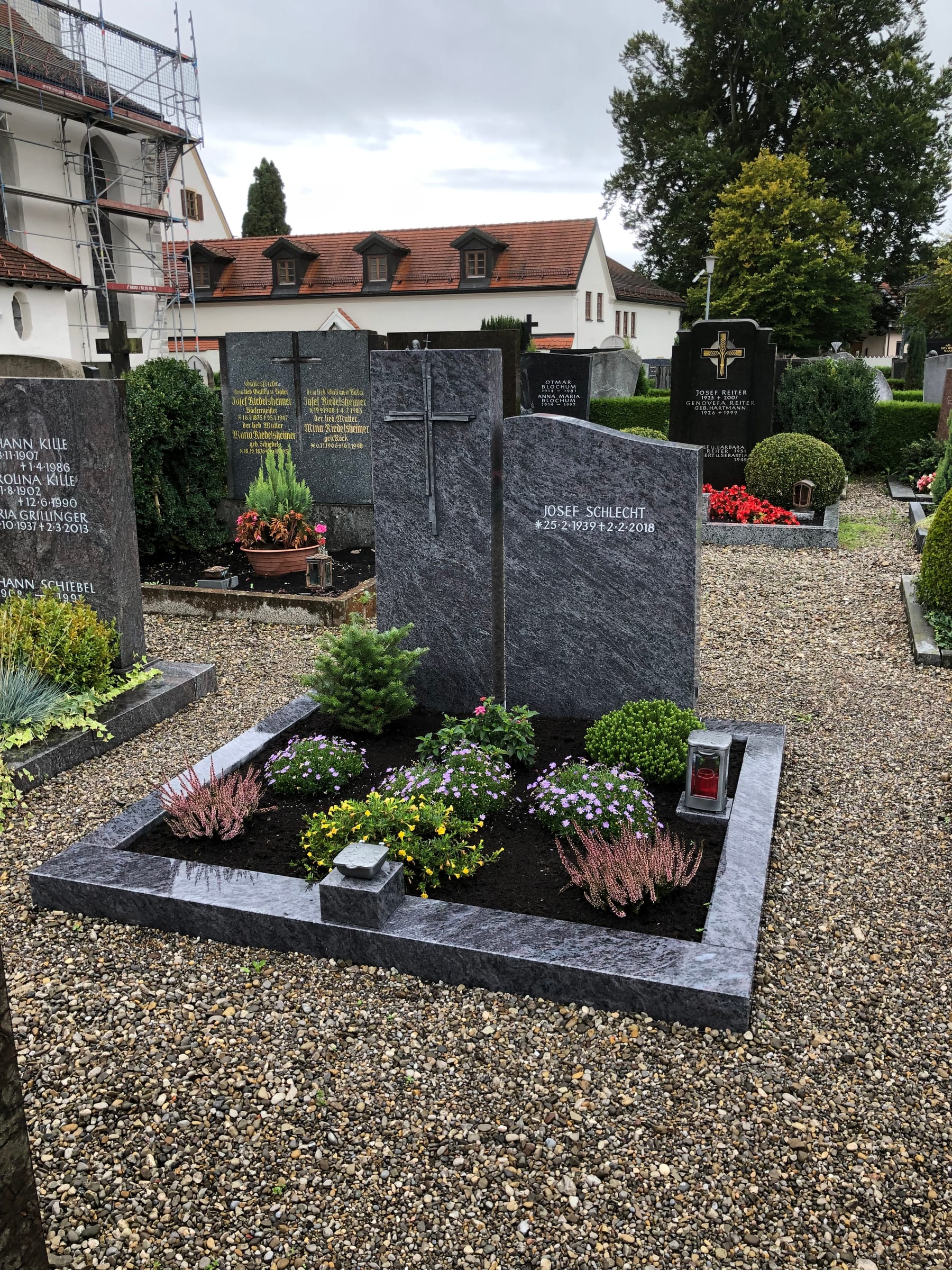 Zweiteiliger Grabstein aus dunkelgrauem Granit mit geschroteter Oberfläche und modernem Metallkreuz
