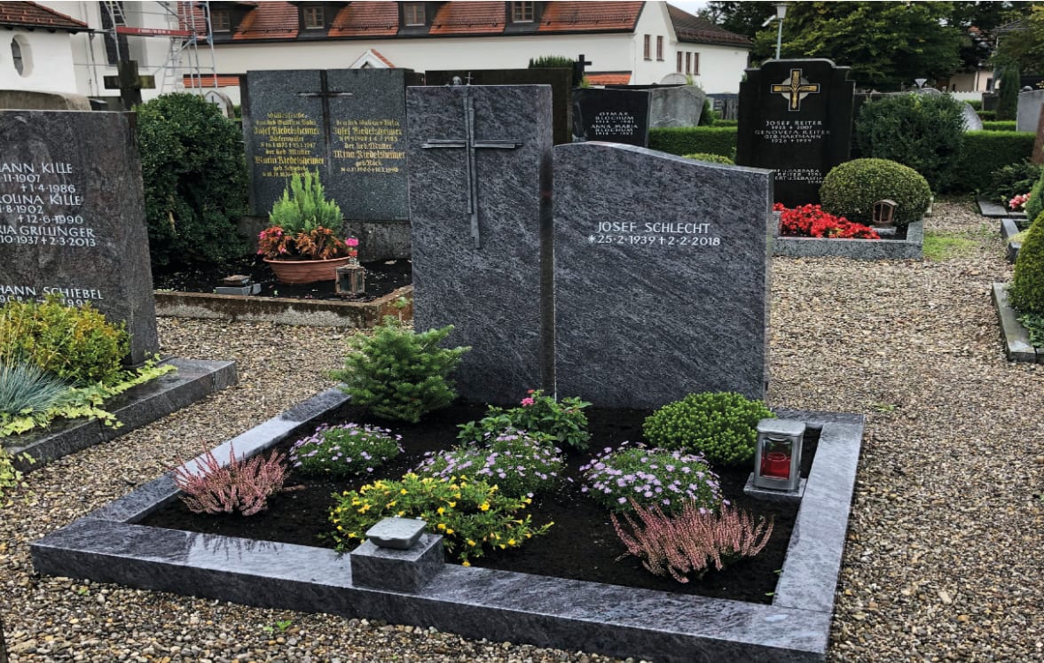 Zweiteiliger Grabstein aus dunkelgrauem Granit mit geschroteter Oberfläche und modernem Metallkreuz