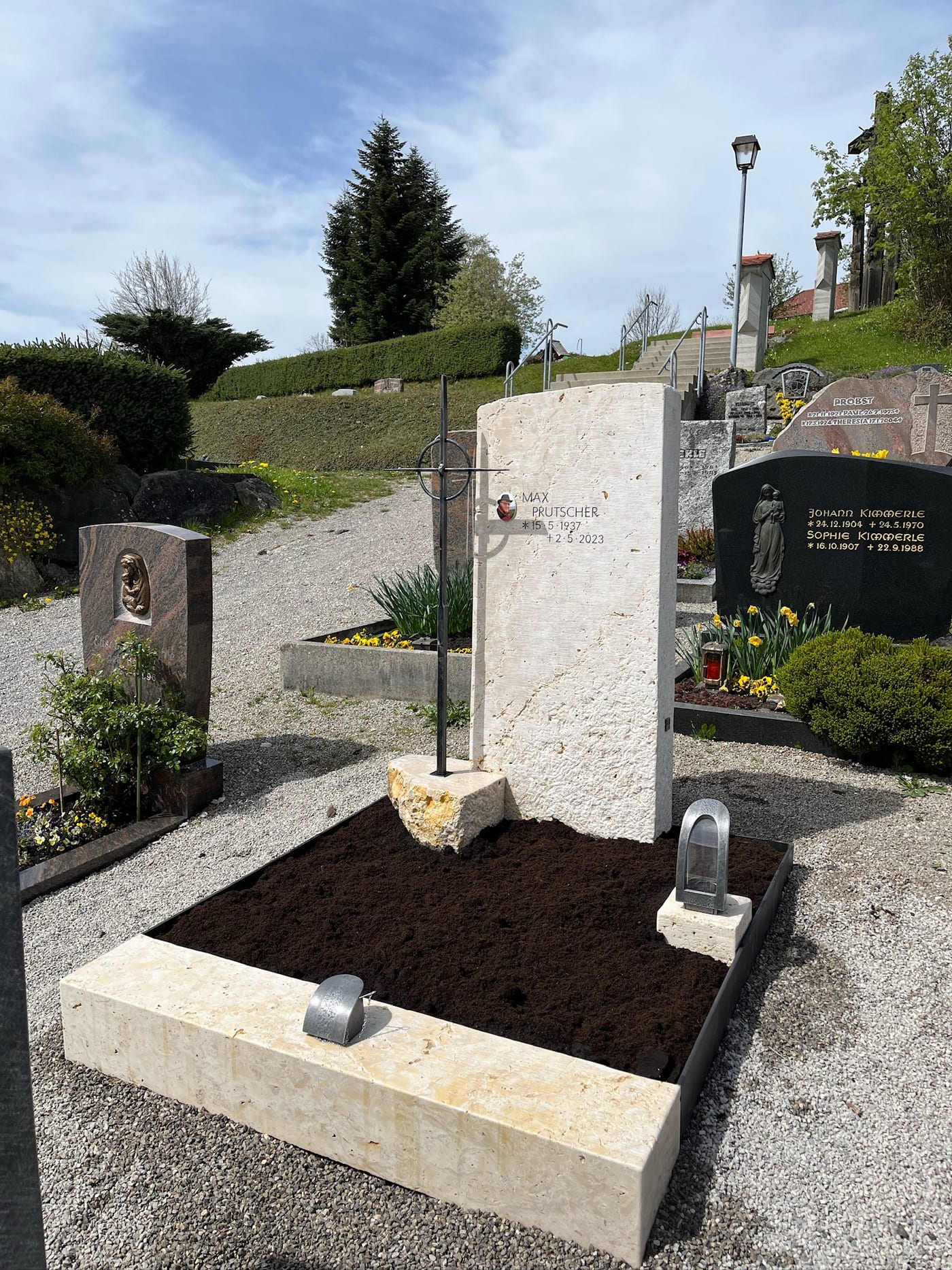 Heller Kalkstein-Grabstein mit schlanker Stele, naturbelassener Spaltbasis und aufgesetztem Metallkreuz – Ansicht 3