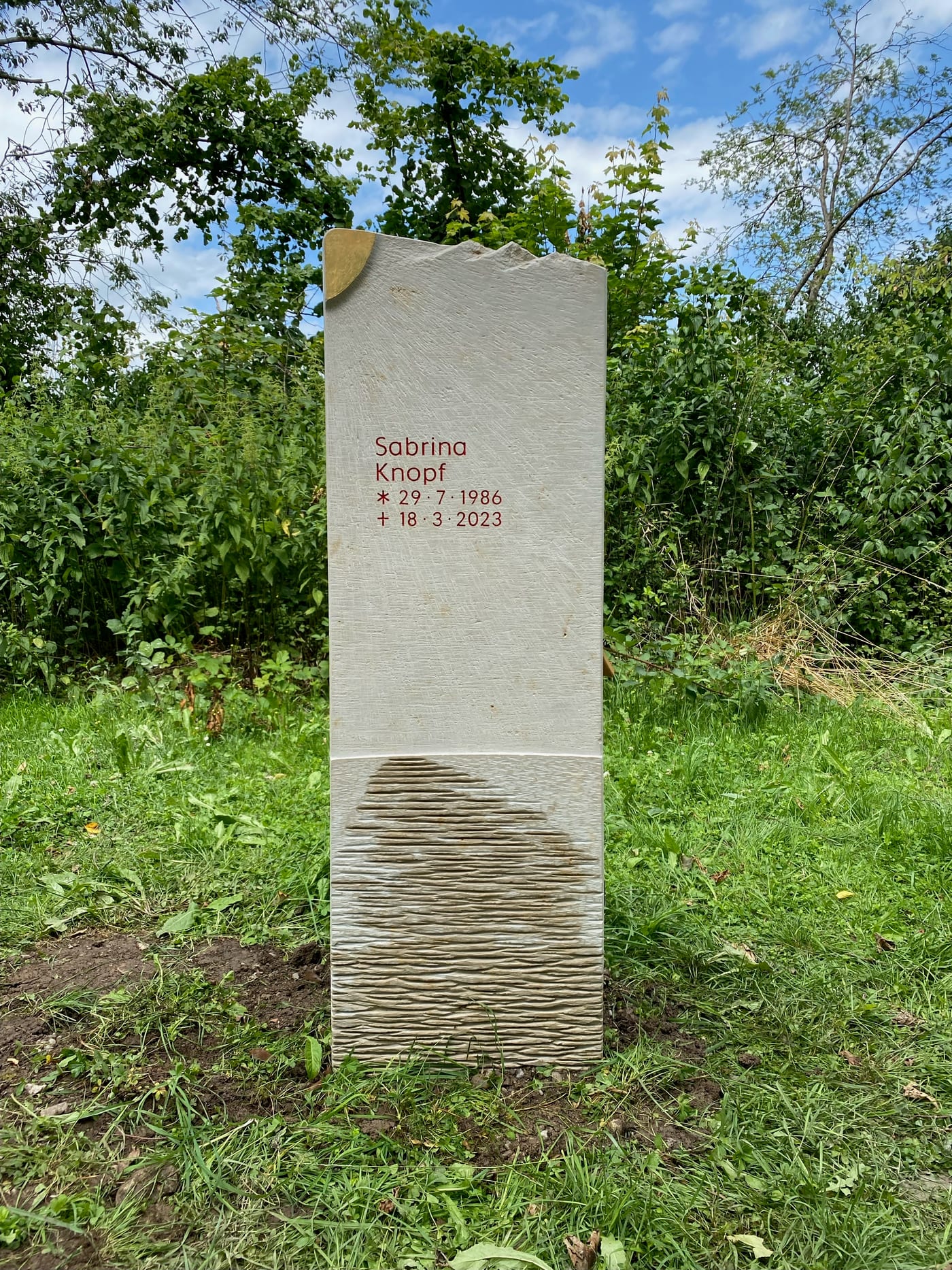 Grabstein aus hellem Naturstein mit feiner Stockhammer-Bearbeitung und vergoldeter Sonnenskulptur in der Steinkrone – Ansicht 3