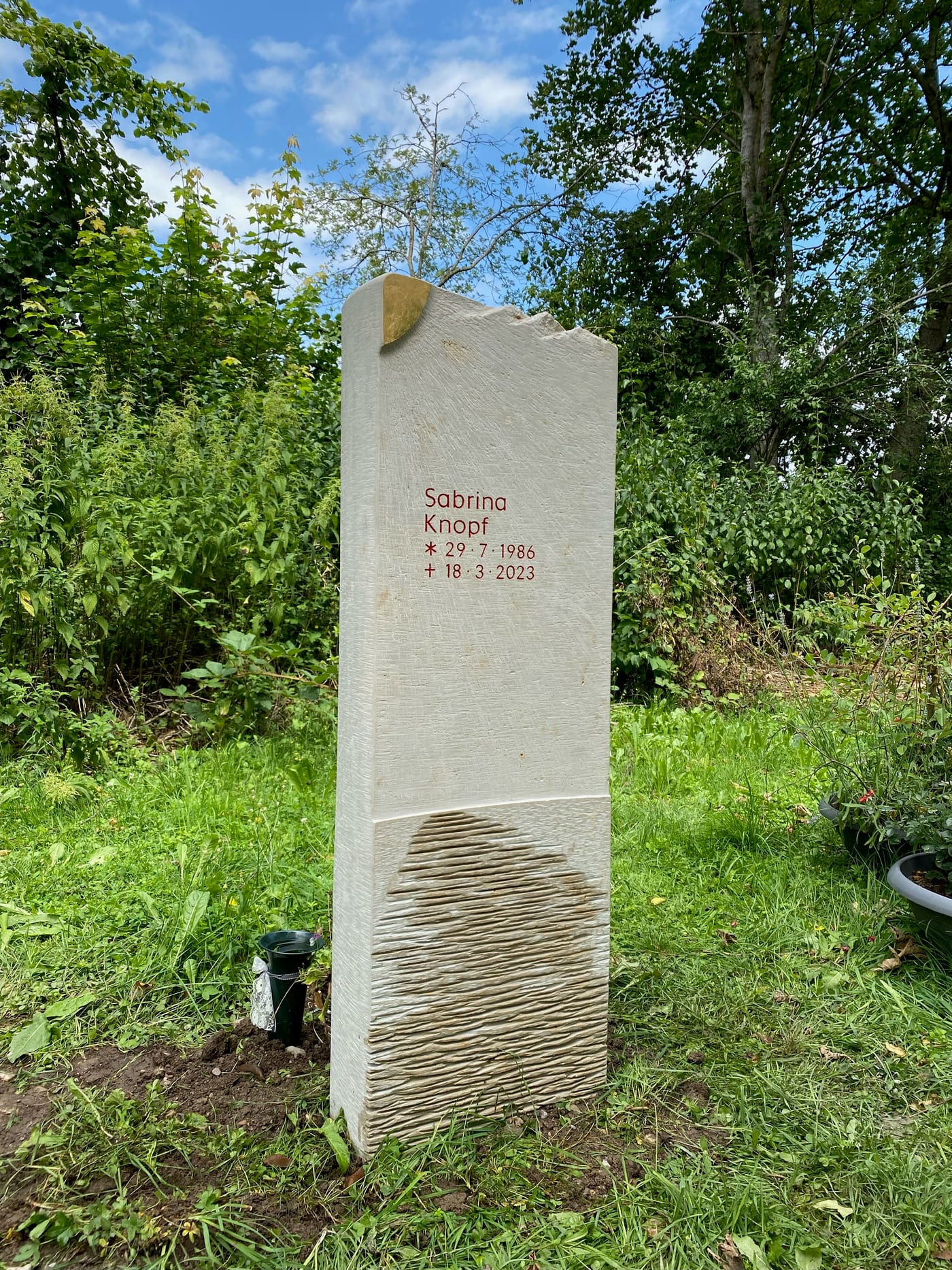 Grabstein aus hellem Naturstein mit feiner Stockhammer-Bearbeitung und vergoldeter Sonnenskulptur in der Steinkrone – Ansicht 4