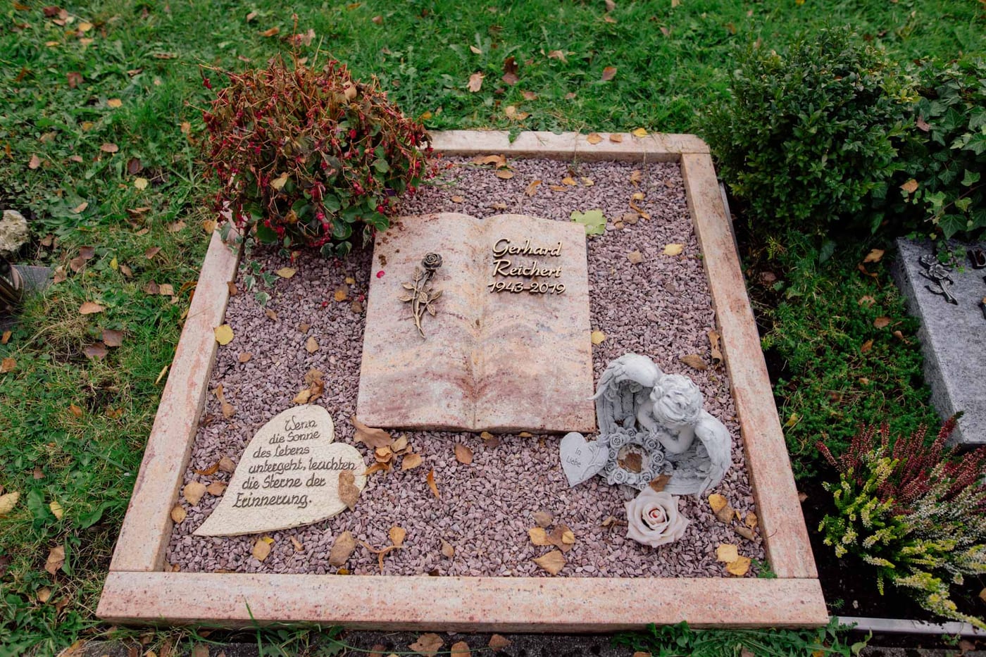 Urnengrab-Liegestein in rosa Naturstein mit Buch-Motiv, Engel-Figur und herzförmigem Stein auf Kiesanlage – Ansicht 2