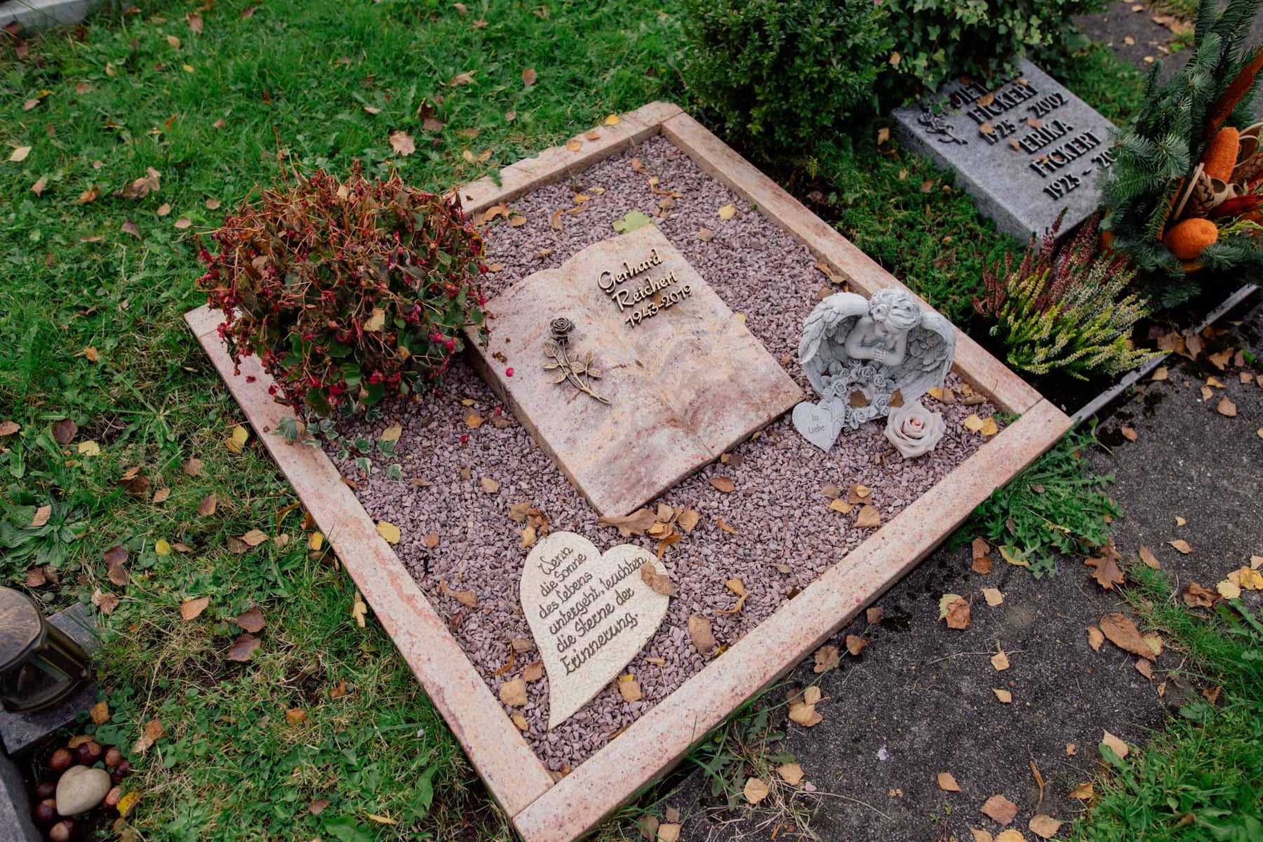 Urnengrab-Liegestein in rosa Naturstein mit Buch-Motiv, Engel-Figur und herzförmigem Stein auf Kiesanlage