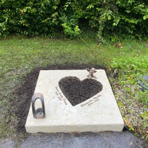 Urnengrab-Liegestein aus hellem Kalkstein mit ausgearbeitetem dunklem Herzmotiv und Bronzeschmetterling